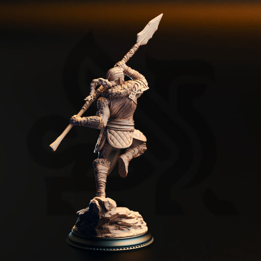 A statue of a warrior figure holding a spear and standing on a rock base against a dark background.