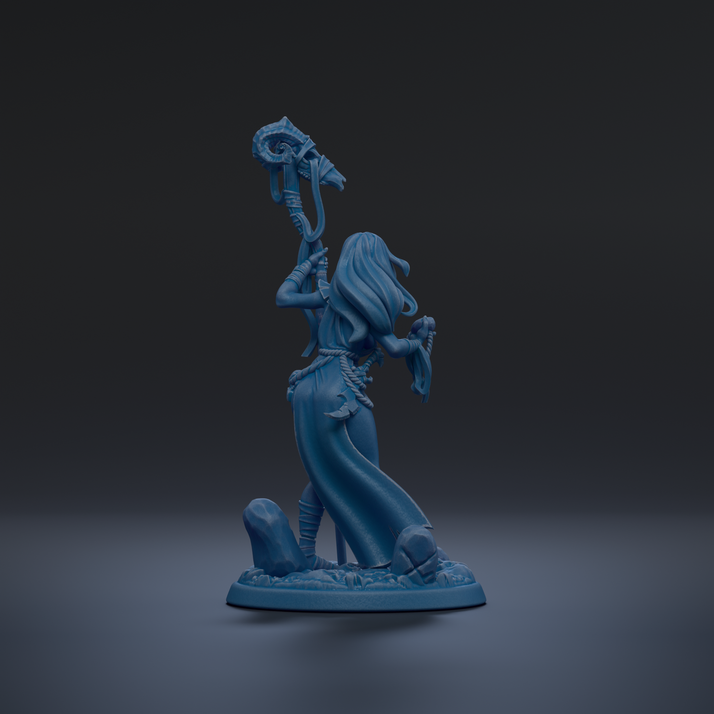 A blue figurine of a woman holding a staff and standing on a rock formation against a dark background.