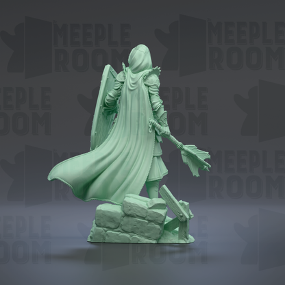 A green statue of a person with a flowing cape and a shield, standing on a rock formation.
