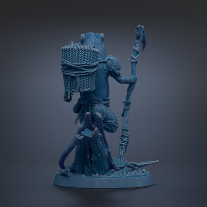 A blue figurine of a fantastical creature, possibly a dragon or serpent, holding a staff and a bundle of items, standing on a rock formation.