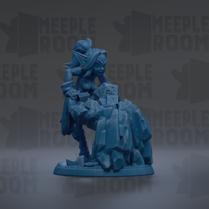 A blue figurine of a female character with a large head and long hair, sitting on a rock formation.