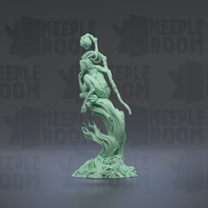 A green, abstract sculpture of a figure with a long, curved arm and a pointed head, standing on a rock formation.