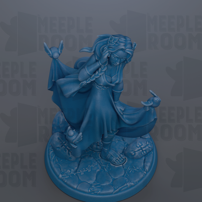 A blue figurine of a woman with long hair and a flowing dress, holding a bird in her hand, standing on a rock formation.