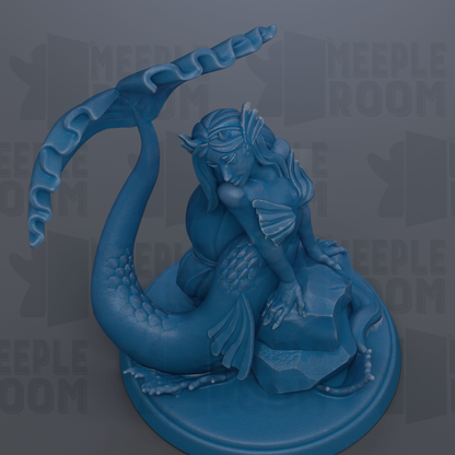 A blue mermaid figurine is sitting on a rock, with a large fin-like structure on its back.