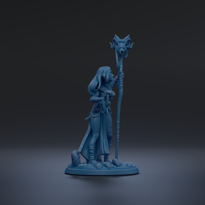 A blue figurine of a woman holding a staff and standing on a rock formation against a dark background.