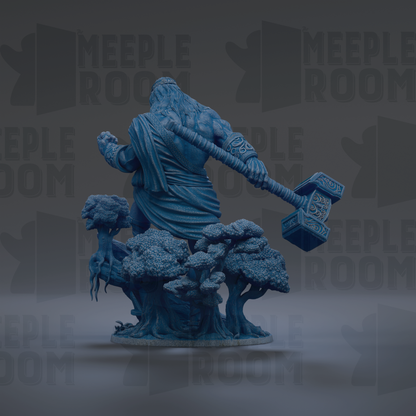 A blue statue of a muscular, bearded figure holding a large hammer, standing on a base with trees and foliage.