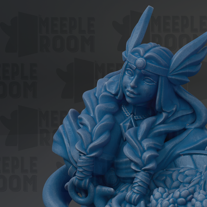 A blue statue of a woman with a headdress and flowing hair, sitting on a rock or pedestal.