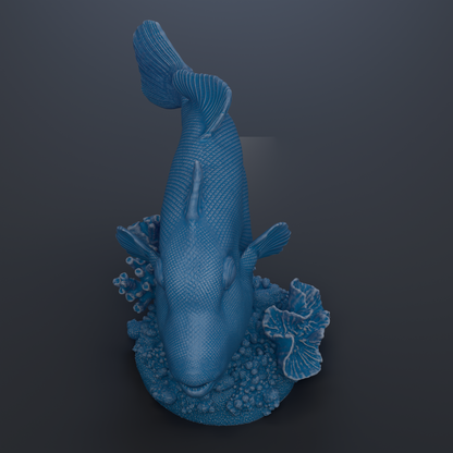A blue fish sculpture is displayed on a dark surface, surrounded by small coral pieces.