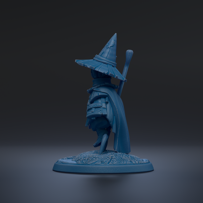 A blue figurine of a wizard or magical character wearing a pointed hat and holding a staff, standing on a base with a floral design.